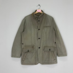 Peut inclure: Une veste utilitaire verte avec un col montant, cinq boutons et plusieurs poches.