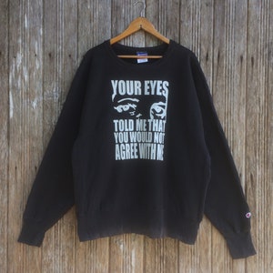Puede incluir: Sudadera negra Champion con un estampado gráfico blanco de un par de ojos y el texto "YOUR EYES TOLD ME THAT YOU WOULD NOT AGREE WITH ME".