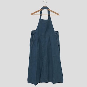 Könnte beinhalten: Ein dunkelblaues Leinen-Overallkleid mit einem Halterneck und verstellbaren Trägern. Das Kleid hat eine lockere Passform und einen leicht ausgestellten Rock.
