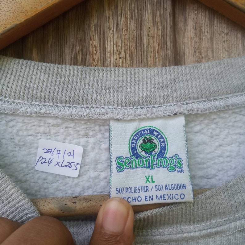 May include: Grey sweatshirt with a white tag that says "Official Wear Senor Frog's MR XL 50% Polyester/50% Algodon Echo en Mexico".