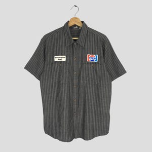 May include: A gray and white striped short-sleeved button-up shirt with a "Generation Next" patch on the left chest and a Pepsi logo patch on the right chest.