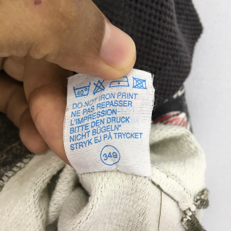 May include: A close-up shot of a white clothing label with blue text and symbols. The label features washing instructions and the text "DO NOT IRON PRINT" in several languages. A small circle with the number "349" is also present.