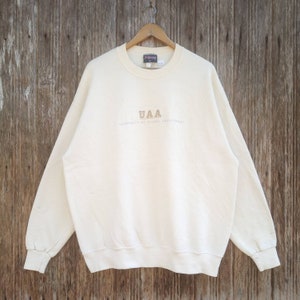 May include: A white sweatshirt with the text "UAA University of Alaska Anchorage" embroidered in brown on the front.