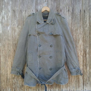 May include: A gray double-breasted coat with a belt and frayed edges. The coat has a collar and four buttons down the front.