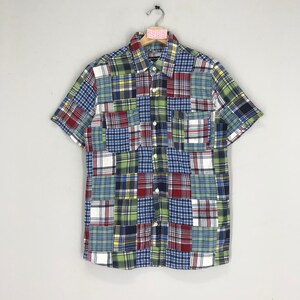 Könnte beinhalten: Ein kurzärmeliges Hemd mit Knöpfen und Patchwork-Muster. Das Hemd besteht aus verschiedenen karierten Stoffen in Blau, Grün, Rot und Weiß.