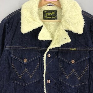 Op de afbeelding: Een donkerblauw denim jack met een lichtbruine sherpa voering. Het jack heeft een knoopsluiting, twee borstzakken en twee voorzakken. Het label op het jack staat "Wrangler Orange Coat".