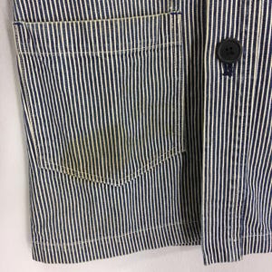 May include: Close-up of a blue and white striped jacket. The jacket features a pocket on the left side and a black button closure. The fabric has a vertical stripe pattern.