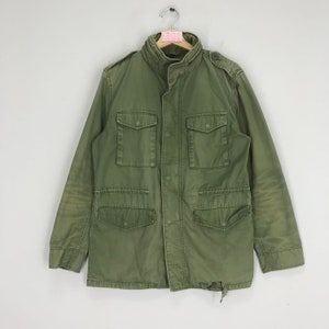 Peut inclure: Une veste utilitaire verte avec un devant boutonné, quatre poches et un col. La veste a un aspect vieilli.
