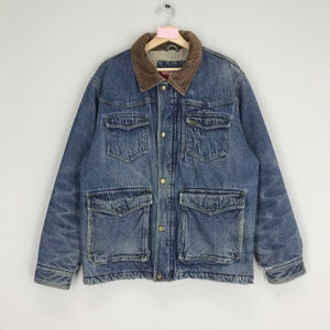 Puede incluir: Una chaqueta vaquera azul con cuello de pana marr&oacute;n y forro de sherpa. La chaqueta tiene dos bolsillos grandes con solapa en la parte delantera y dos bolsillos m&aacute;s peque&ntilde;os en el pecho. La chaqueta tiene cierre de botones y cierre de cremallera.