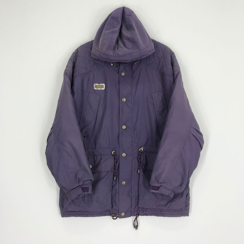 May include: A purple hooded jacket with a button-up front, drawstrings, and a small rectangular patch. The jacket has a relaxed fit and features pockets and adjustable cuffs. The jacket is made of a durable material.