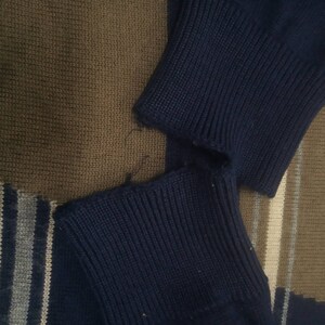 May include: Close-up of a navy blue knitted sweater with a frayed edge. The sweater is made of a soft, comfortable material.