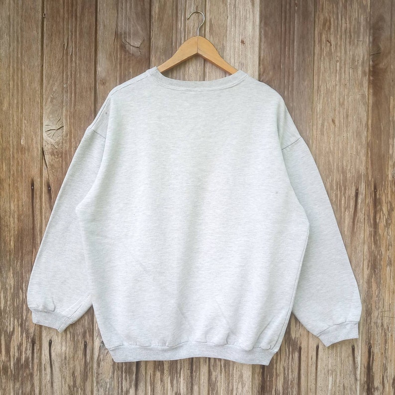 May include: A grey sweatshirt with long sleeves and a crew neck. The sweatshirt is hanging on a wooden hanger.