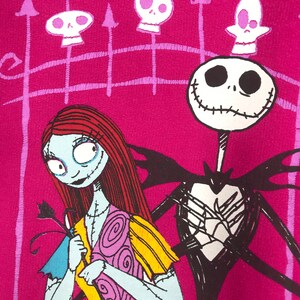 Puede incluir: Un fondo rosa con una ilustraci&oacute;n en blanco y negro de Jack Skellington de Pesadilla Antes de Navidad. Lleva un traje negro y tiene una sonrisa cosida. Sally, una mu&ntilde;eca de trapo con el pelo rojo, est&aacute; de pie a la izquierda de Jack. Lleva un vestido amarillo y rosa. Hay calaveras blancas y negras sobre un fondo rosa en las esquinas superiores de la imagen.