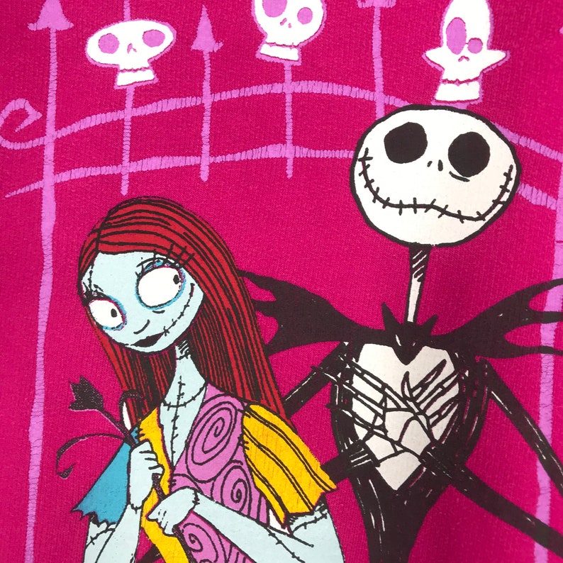Puede incluir: Un fondo rosa con una ilustraci&oacute;n en blanco y negro de Jack Skellington de Pesadilla Antes de Navidad. Lleva un traje negro y tiene una sonrisa cosida. Sally, una mu&ntilde;eca de trapo con el pelo rojo, est&aacute; de pie a la izquierda de Jack. Lleva un vestido amarillo y rosa. Hay calaveras blancas y negras sobre un fondo rosa en las esquinas superiores de la imagen.
