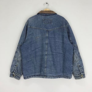 Puede incluir: Una chaqueta vaquera azul con cuello de pana marr&oacute;n. La chaqueta tiene un bolsillo de parche en la espalda y dos bolsillos de solapa en el pecho.