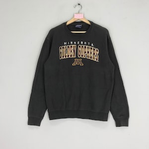 May include: A dark gray sweatshirt with the words "MINNESOTA GOLDEN GOPHERS" in gold and white lettering. Below the text is a gold "M" logo. The sweatshirt has a crew neck and long sleeves.