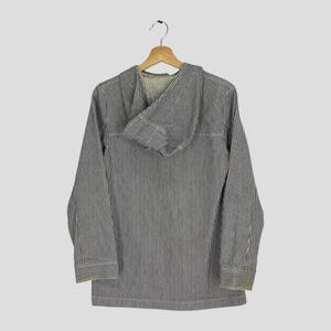 May include: A long-sleeved hooded jacket with vertical black and white stripes. The jacket is hanging on a wooden hanger. The hood is folded down, revealing the interior lining. The jacket has a classic, casual style.