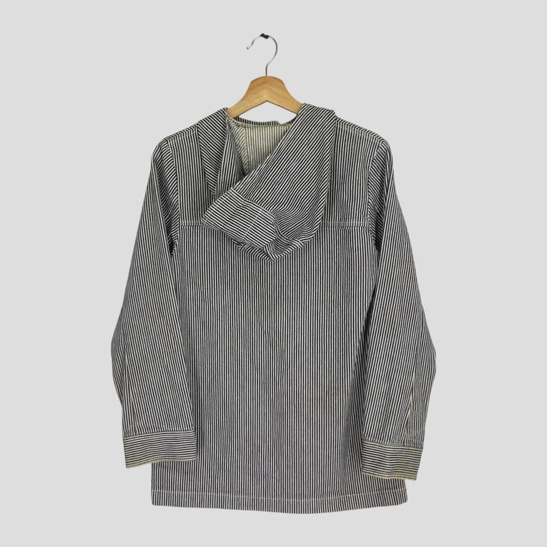 May include: A long-sleeved hooded jacket with vertical black and white stripes. The jacket is hanging on a wooden hanger. The hood is folded down, revealing the interior lining. The jacket has a classic, casual style.