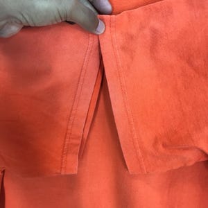 Pu&ograve; includere: Primo piano della cucitura di una maglietta arancione. La cucitura &egrave; realizzata con un punto dritto.
