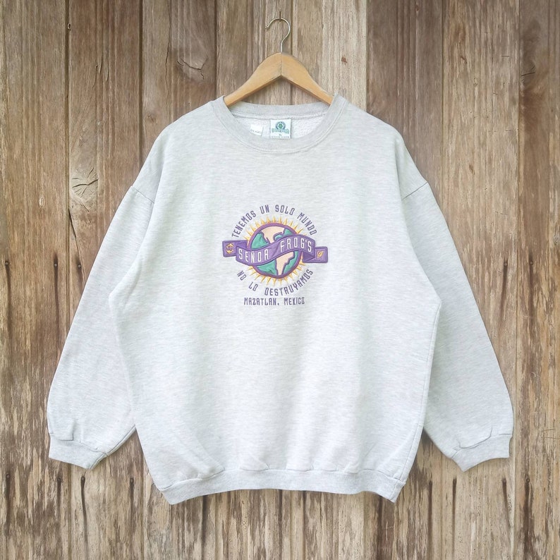 May include: A grey sweatshirt with a graphic print of a globe with the text "Tenemos un solo mundo" and "Senor Frogs" in a purple banner. The text "No lo destruvamos" and "Mazatlan, Mexico" are also printed on the sweatshirt.