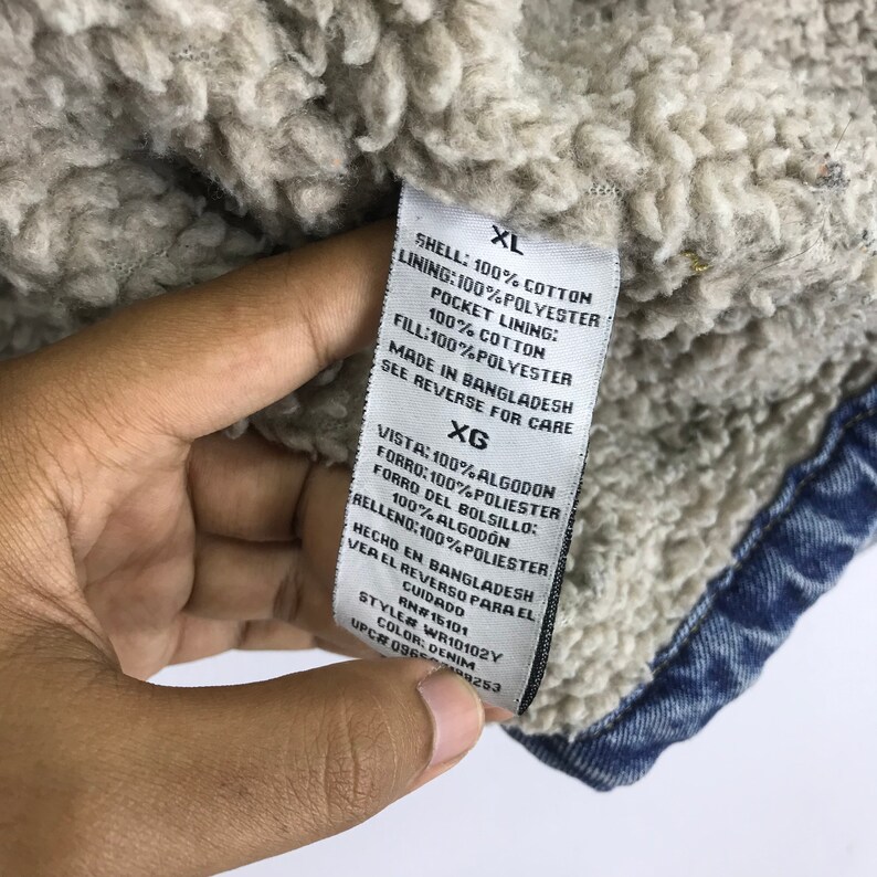 Puede incluir: Una chaqueta vaquera azul con forro de sherpa. La etiqueta dice "XL" y enumera el contenido de la tela como 100% algod&oacute;n para la c&aacute;scara, 100% poli&eacute;ster para el forro, 100% algod&oacute;n para el forro del bolsillo y 100% poli&eacute;ster para el relleno. La etiqueta tambi&eacute;n dice "Hecho en Bangladesh" y "Ver el reverso para el cuidado".