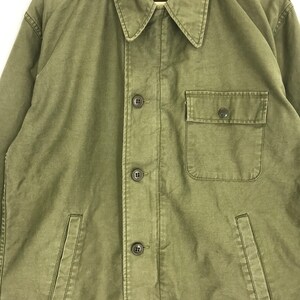 May include: Olive green jacket with a button-up front, a collared neckline, and a single chest pocket. The jacket has two side pockets and a relaxed fit. The fabric appears to be a durable, possibly canvas material.
