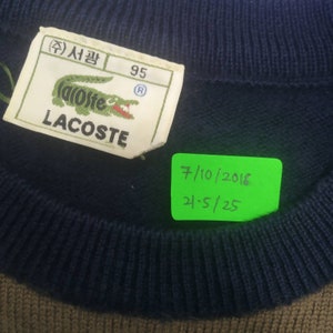 May include: A navy blue Lacoste sweater with a green crocodile logo and the text "(주) 삽 95" on the tag. The sweater has a brown ribbed trim at the bottom.