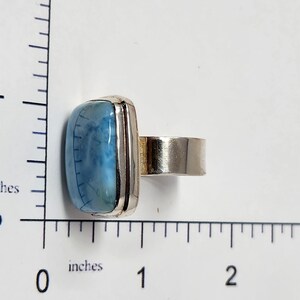 May include: A silver ring featuring a rectangular, light blue gemstone with a marbled appearance. The gemstone is approximately 1 inch long. The ring has a wide band and a simple, modern design, suitable for everyday wear.
