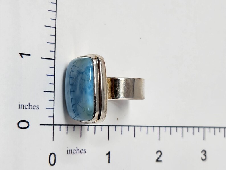 May include: A silver ring featuring a rectangular, light blue gemstone with a marbled appearance. The gemstone is approximately 1 inch long. The ring has a wide band and a simple, modern design, suitable for everyday wear.