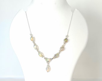 May include: A silver necklace featuring oval-shaped opals. The necklace has a delicate chain and a pendant with a teardrop-shaped opal. The opals have a play of color, with flashes of yellow, orange, and green.