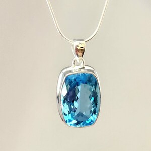 May include: A silver pendant necklace featuring a large, rectangular, light blue gemstone. The gemstone is set in a silver bezel and hangs from a delicate silver chain. The pendant has a polished, reflective surface.