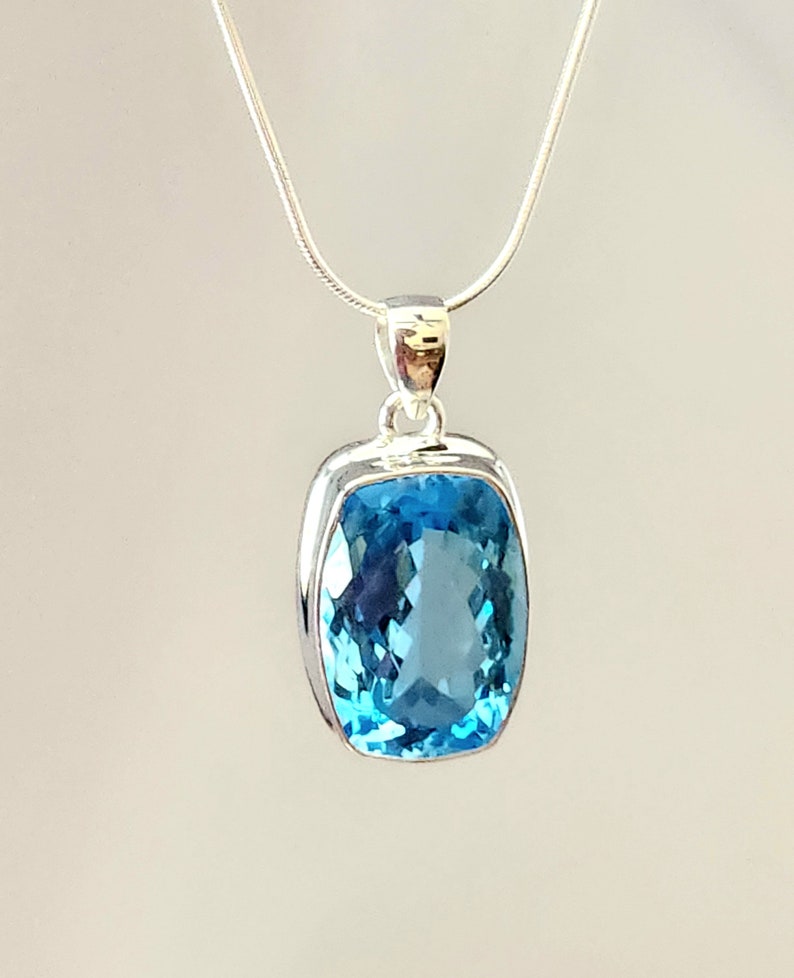 May include: A silver pendant necklace featuring a large, rectangular, light blue gemstone. The gemstone is set in a silver bezel and hangs from a delicate silver chain. The pendant has a polished, reflective surface.