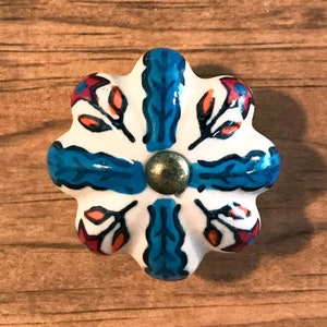 May include: A white ceramic cabinet knob with a blue and orange floral design. The knob has a gold metal center.