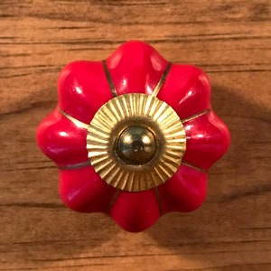May include: A red ceramic cabinet knob with a gold center and a flower-shaped design.