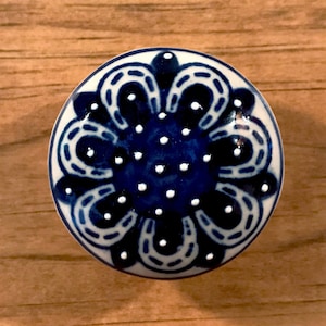May include: A blue and white ceramic knob with a floral design. The knob has a white background with a blue floral pattern and white dots.