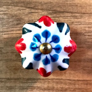 May include: A white ceramic knob with a blue and red floral design. The knob has a gold center and a star-shaped base.