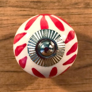 May include: White ceramic knob with a red and white striped pattern and a silver metal base.