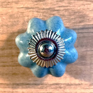 May include: A light blue ceramic cabinet knob with a silver, scalloped trim. The knob has a distressed, crackled finish.