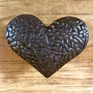 May include: A dark brown heart-shaped metal door knob with a textured surface.