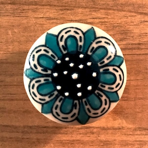 May include: A round ceramic knob with a blue and white floral design. The center of the flower is black with white dots.
