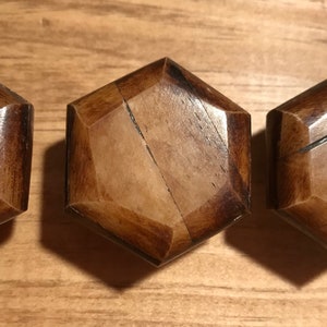May include: Three hexagonal wooden knobs with a dark brown stain. The knobs have a slightly raised, geometric design.