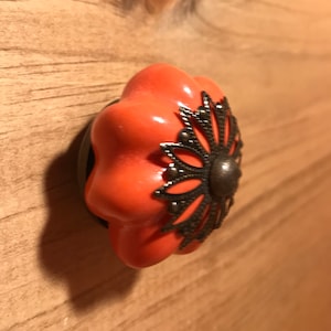 May include: A coral-colored ceramic drawer knob with a decorative metal flower design.