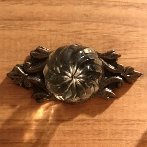 May include: A clear glass knob with a swirl design, mounted on a silver metal base with ornate scrollwork.