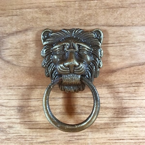 May include: A gold lion head door knocker with a ring pull. The lion head is detailed with a mane and a textured finish.