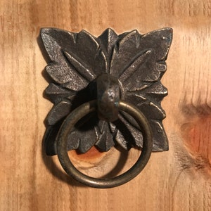 May include: A decorative metal ring pull with a detailed floral design. The ring pull is made of a dark metal with a brass finish.