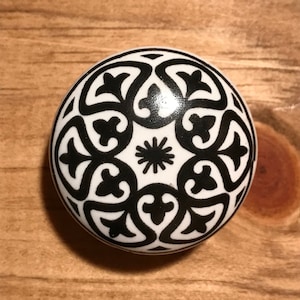May include: A white ceramic knob with a black intricate floral design. The knob is round and has a smooth surface.
