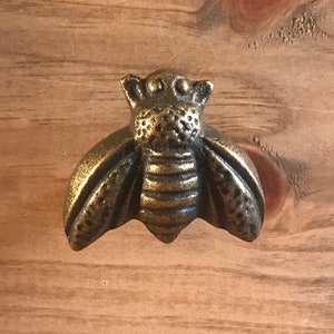 May include: A gold-toned metal bee-shaped drawer pull. The bee has a detailed design with wings, legs, and a segmented body.