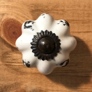 May include: White ceramic knob with a black metal center. The knob has a distressed look with black paint splatters.