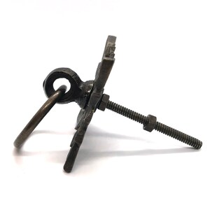 May include: A black metal cabinet pull with a decorative design and a ring handle. The pull has a screw for mounting.