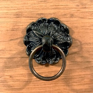 May include: A black metal drawer pull with a decorative floral design and a ring handle.